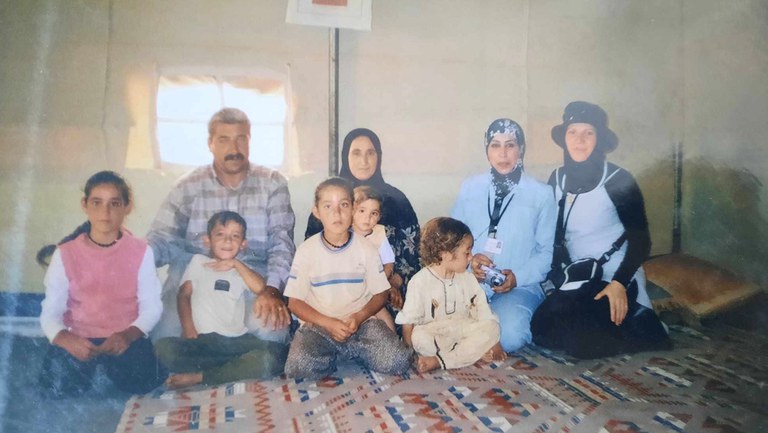 Shahen and her family kneeling on a rug inside a refugee tent.